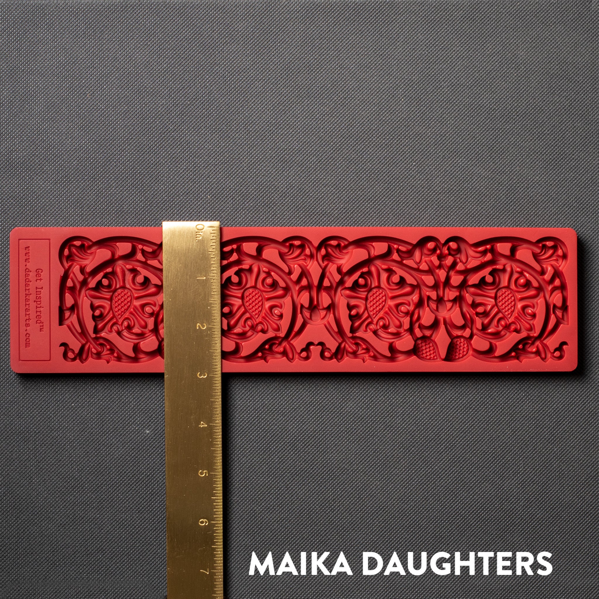 A red silicone mold of an ornate border is against a dark grey background. A gold ruler reding 3 inches width sits on the mold.