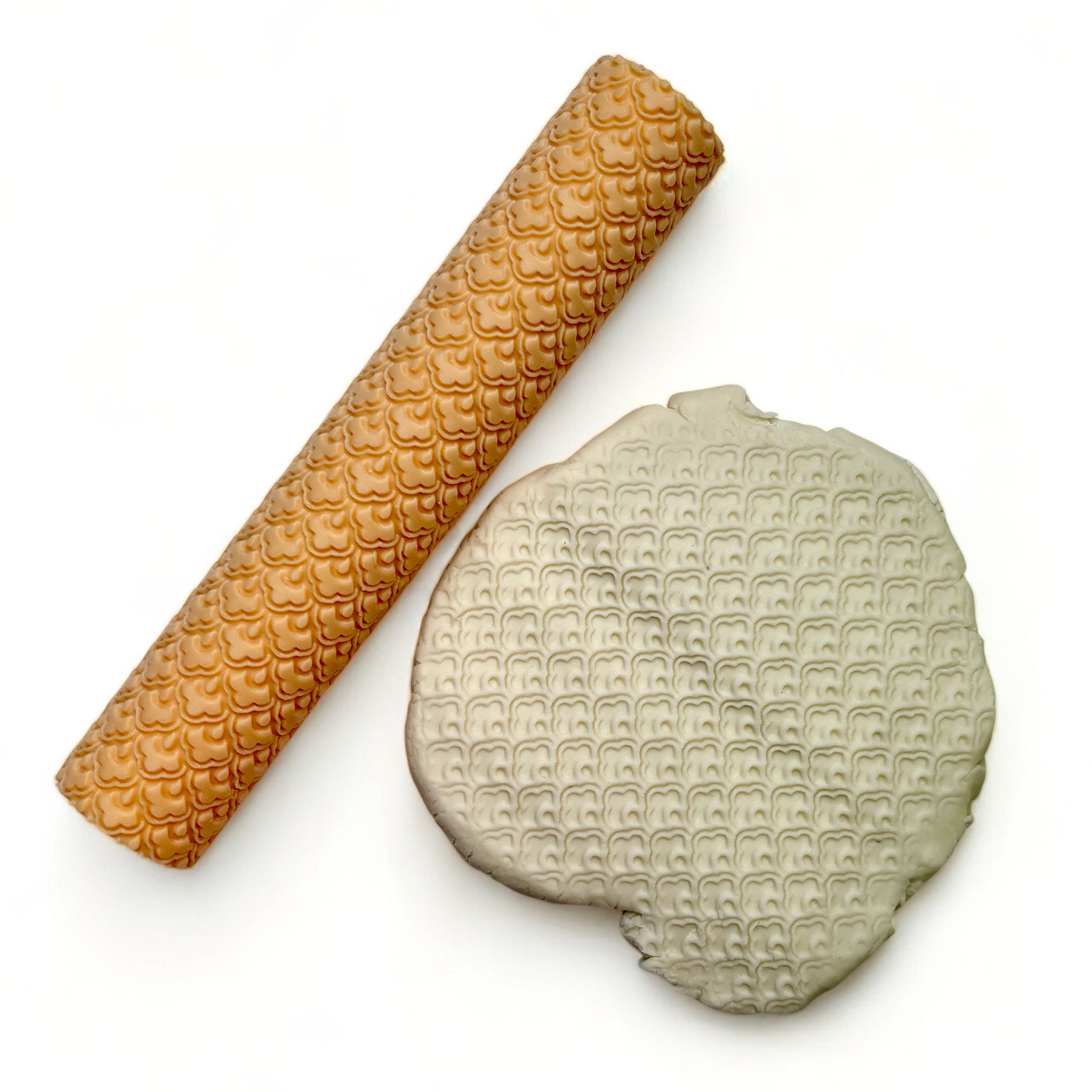 A seamless texture roller and flattened chunk of clay featuring a scallop floral pattern are against a white background.
