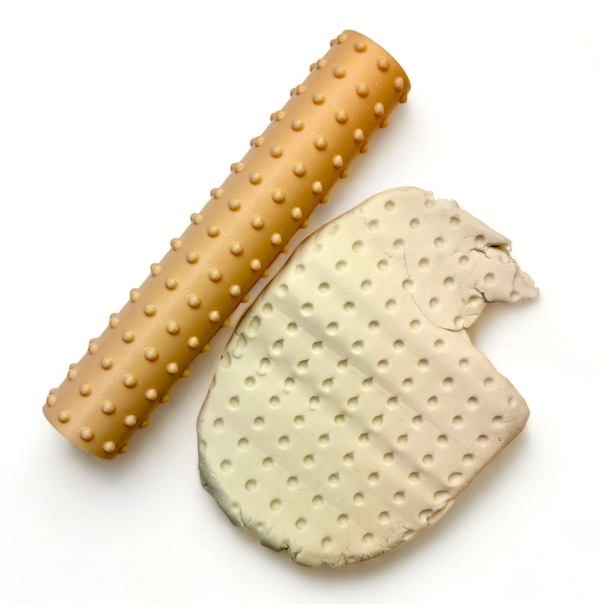 A seamless texture roller and flattened chunk of clay featuring a repeating dot pattern are against a white background.