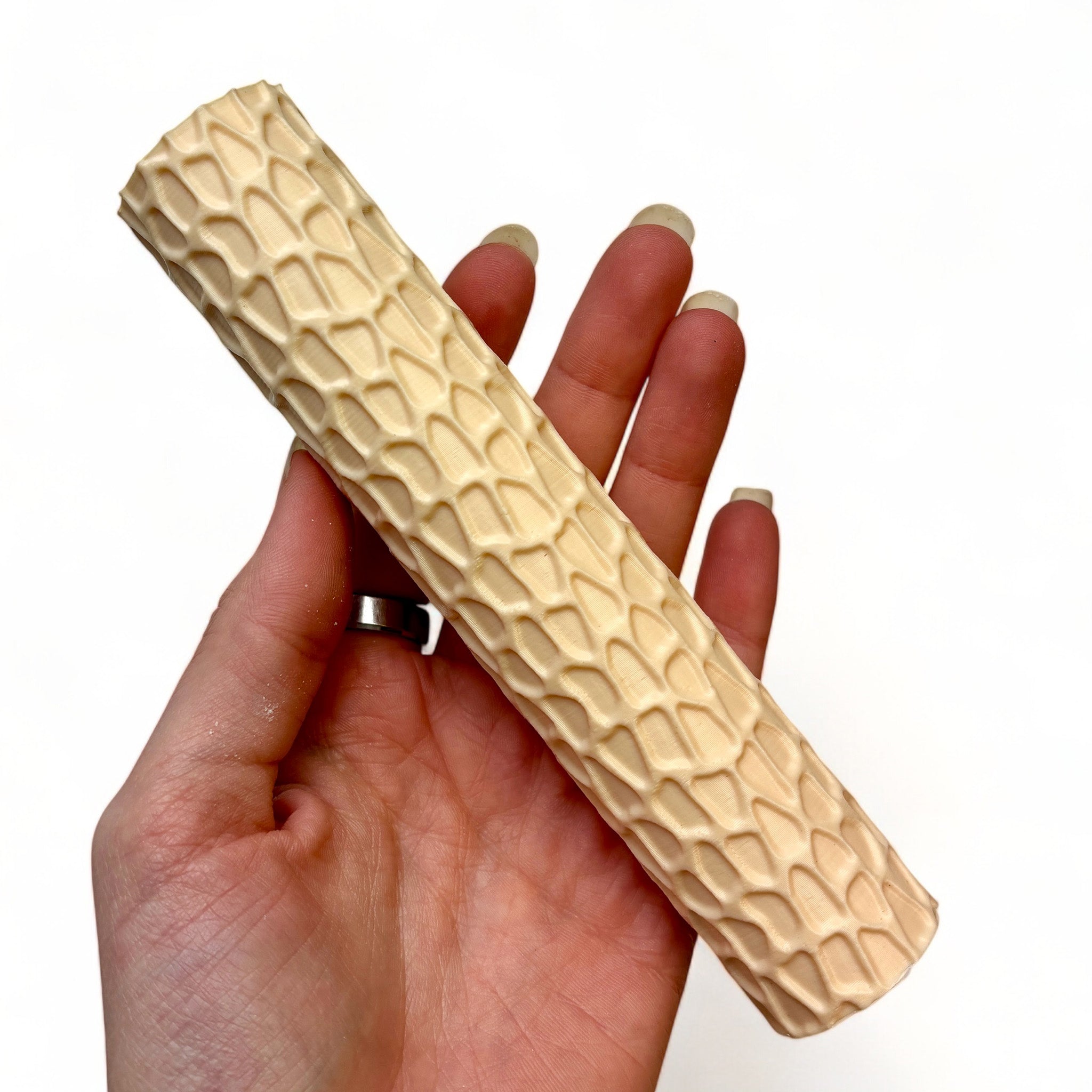 A hand is shown holding Dadakar Art's Stone Path Texture Roller against a white background.
