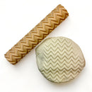 A seamless texture roller and flattened chunk of clay featuring a zig zag pattern are against a white background.
