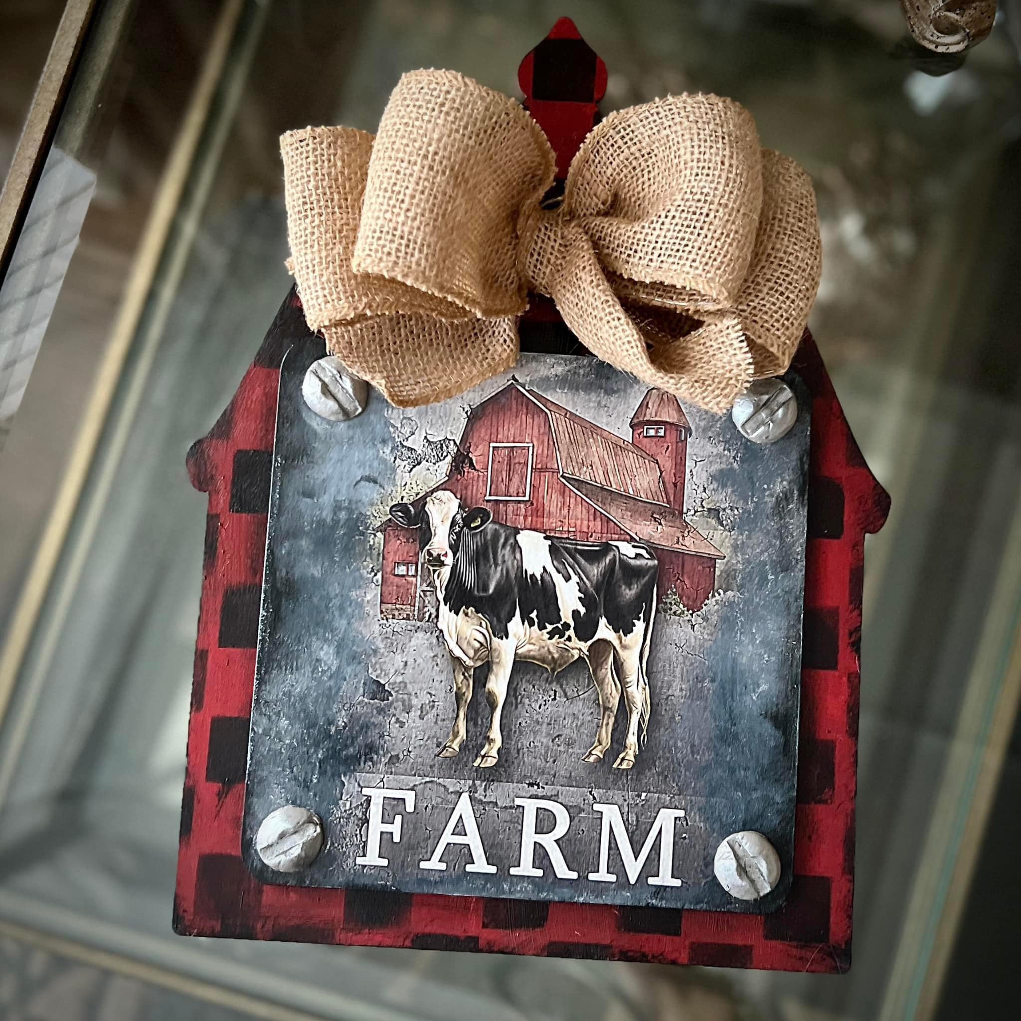 A red and black plaid barn shaped wood craft has a burlap bow and a metal plate that features Decoupage Queen's Farmhouse Signs 4 Pack rice paper on it.