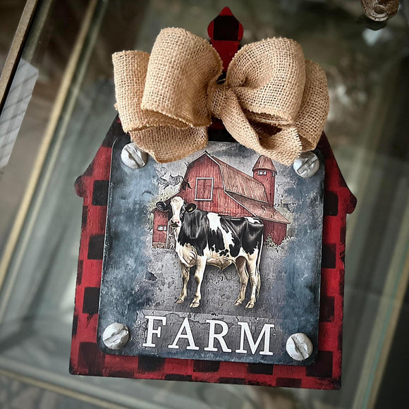 A barn shaped wood craft painted with red and black plaid and a burlap bow features Decoupage Queen's Welcome to the Farm rice paper.