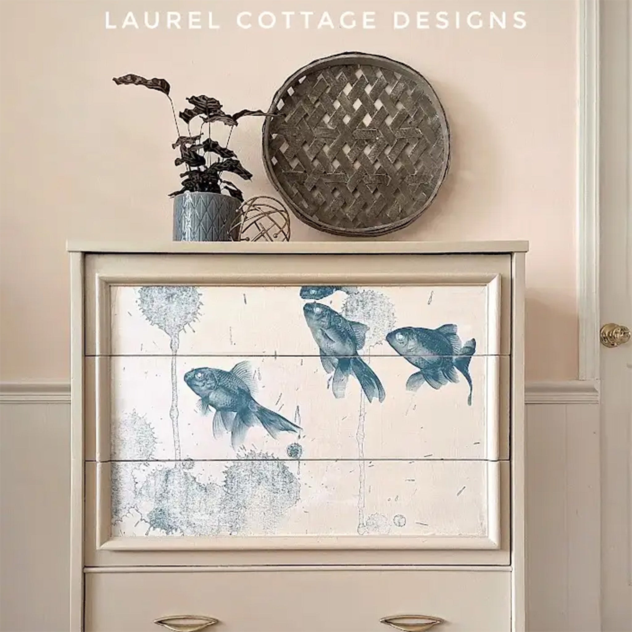 A close-up of a chest of drawers refurbished by Laurel Cottage Designs is painted light beige and features Mint by Michelle's Blue Fish decoupage paper on the top 3 drawers.