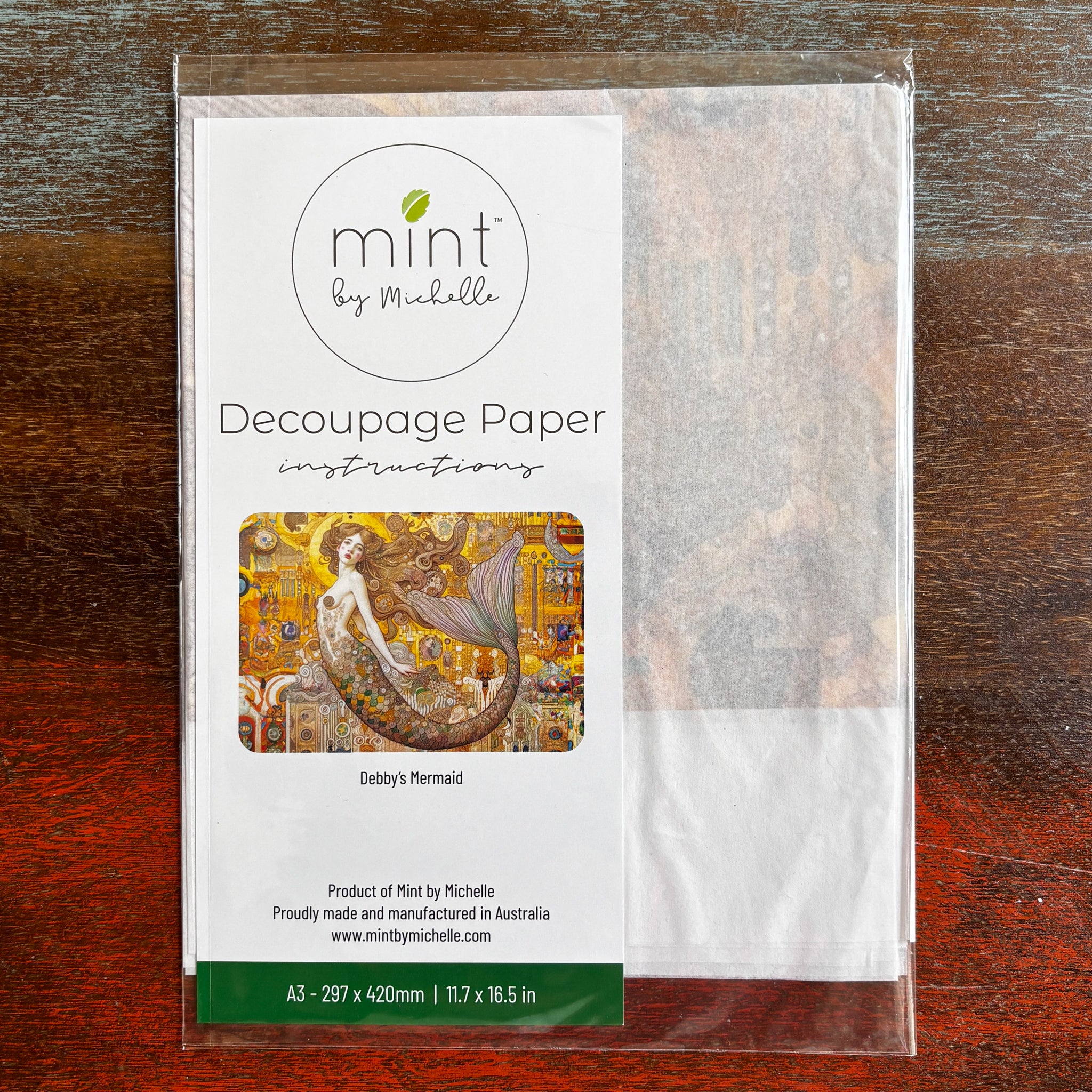 A package of Mint by Michelle's Debby's Mermaid A3 decoupage paper is against a dark wood background.