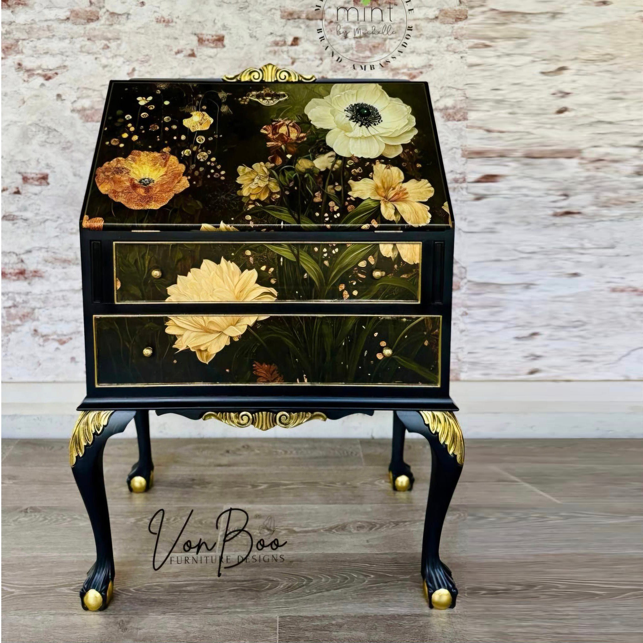 A vintage secretary desk refurbished by Von Boo Furniture Designs is painted black with gold accents and features Mint by Michelle's Flowers Horizontal decoupage paper on it.