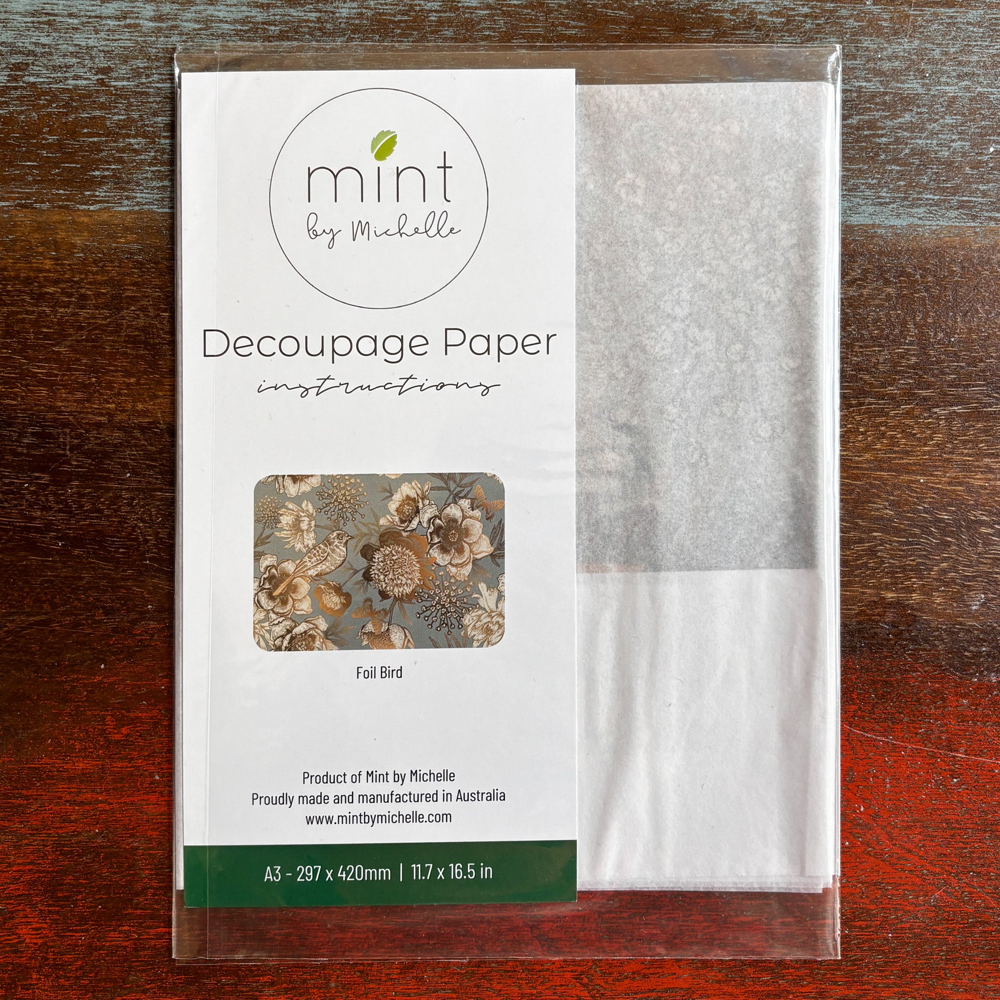 A package of Mint by Michelle's Foil Birds A3 decoupage paper is against a dark wood background.