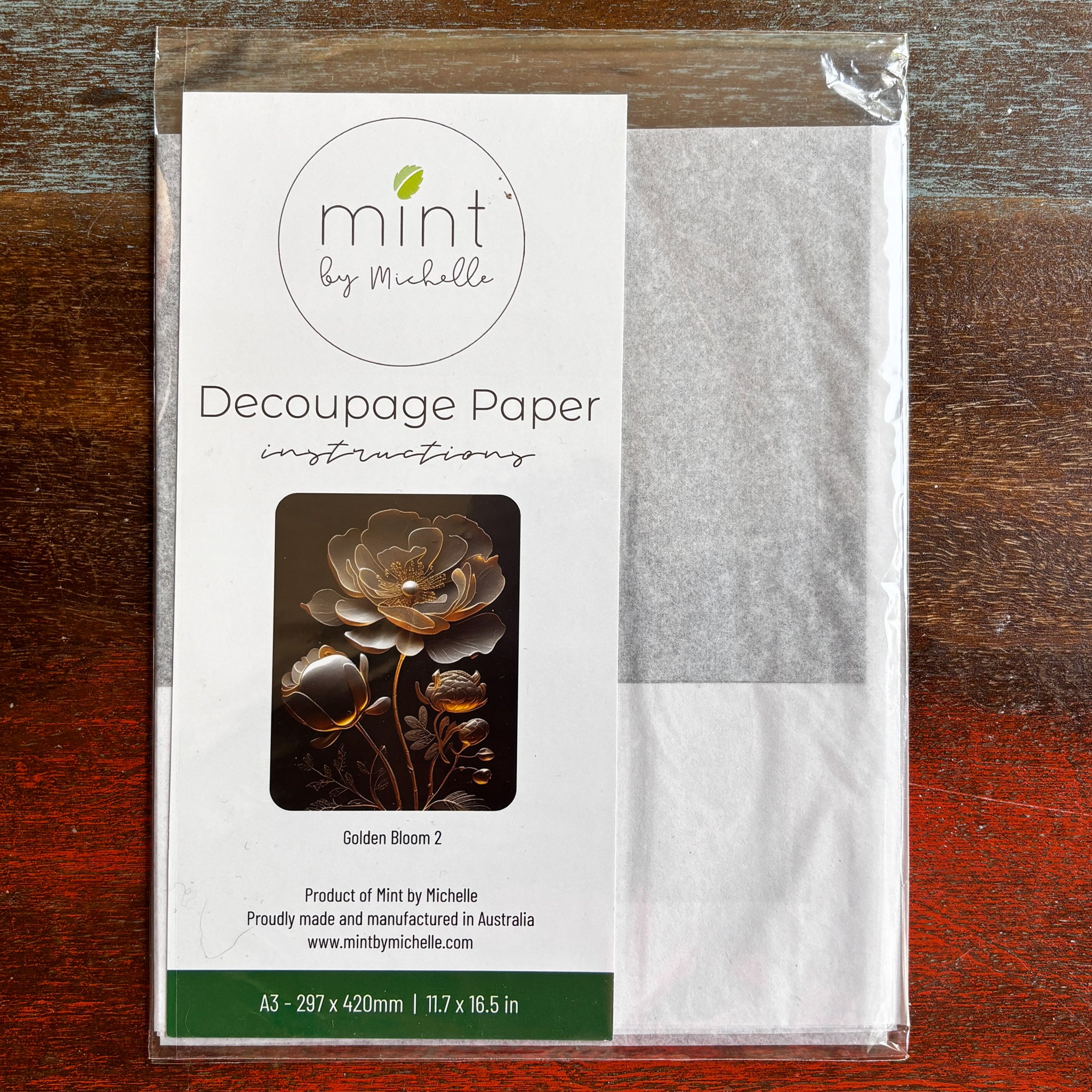 A package of Mint by Michelle's Golden Bloom 2 A3 decoupage paper is against a dark wood background.