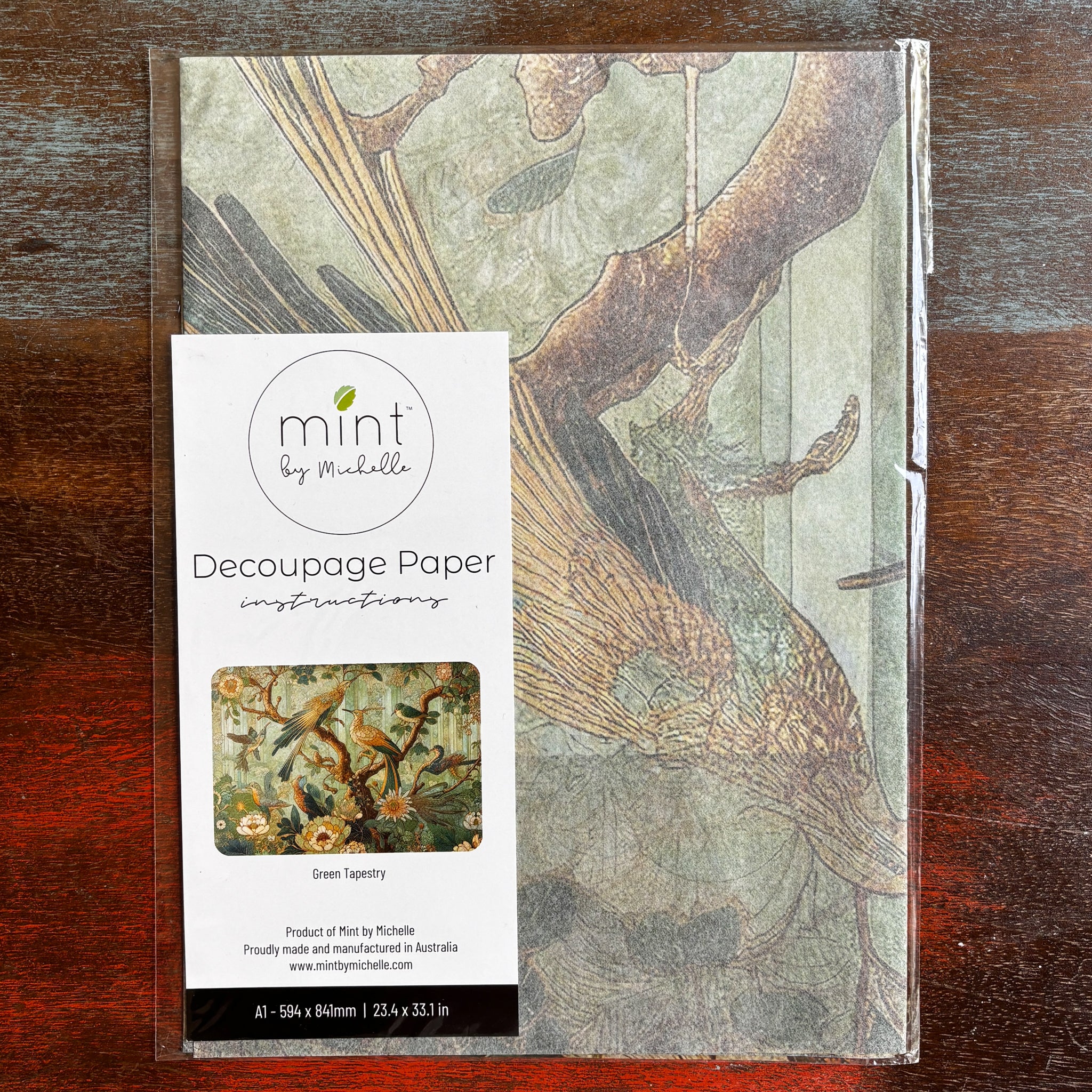 A package of Mint by Michelle's Green Tapestry A1 decoupage paper is against a dark wood background.