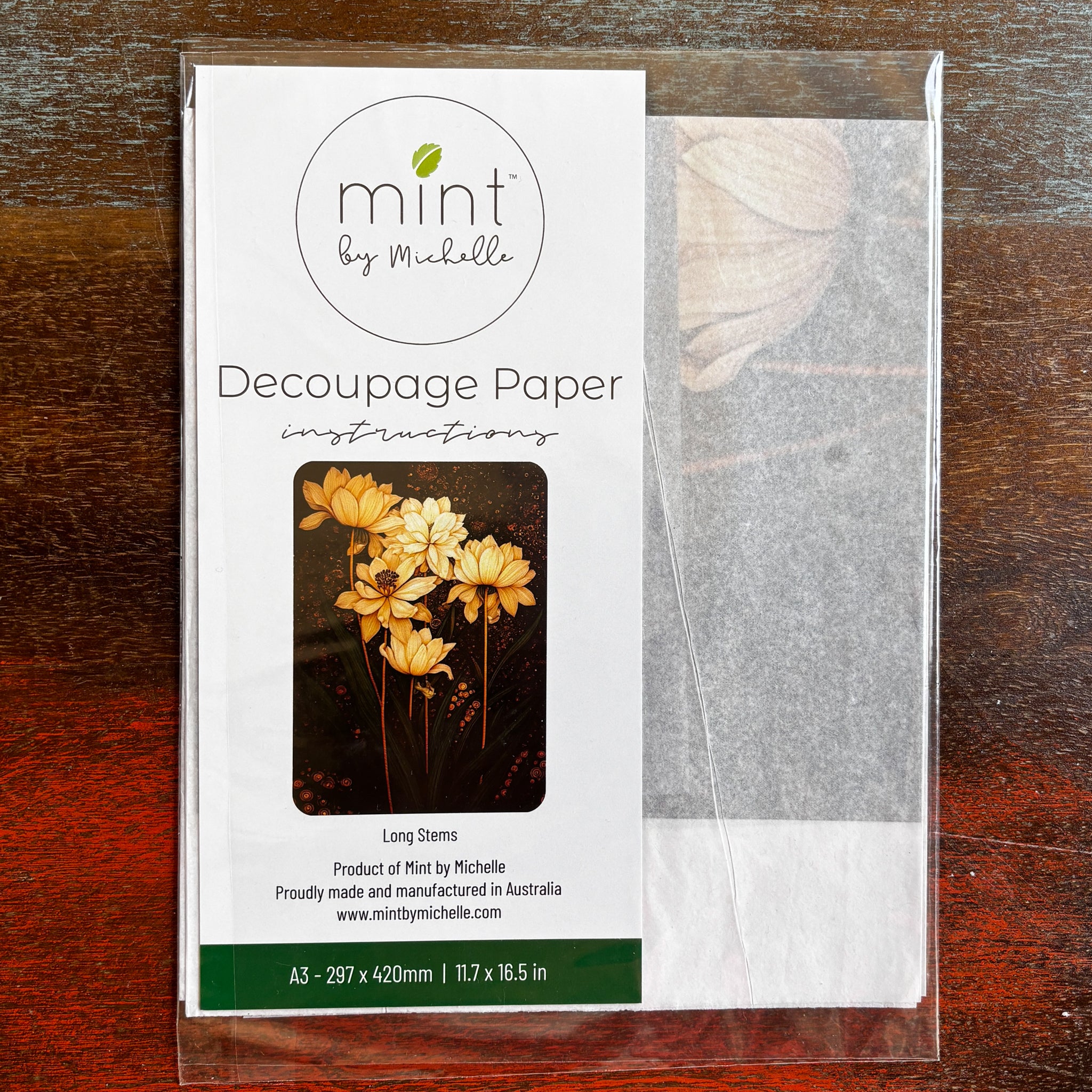 A package of Mint by Michelle's Long Stems A3 decoupage paper is against a dark wood background.