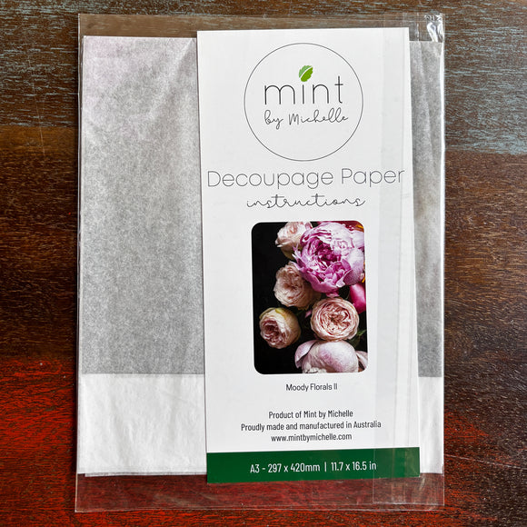 A package of Mint by Michelle's Moody Florals 2 A3 decoupage paper is against a dark wood background.