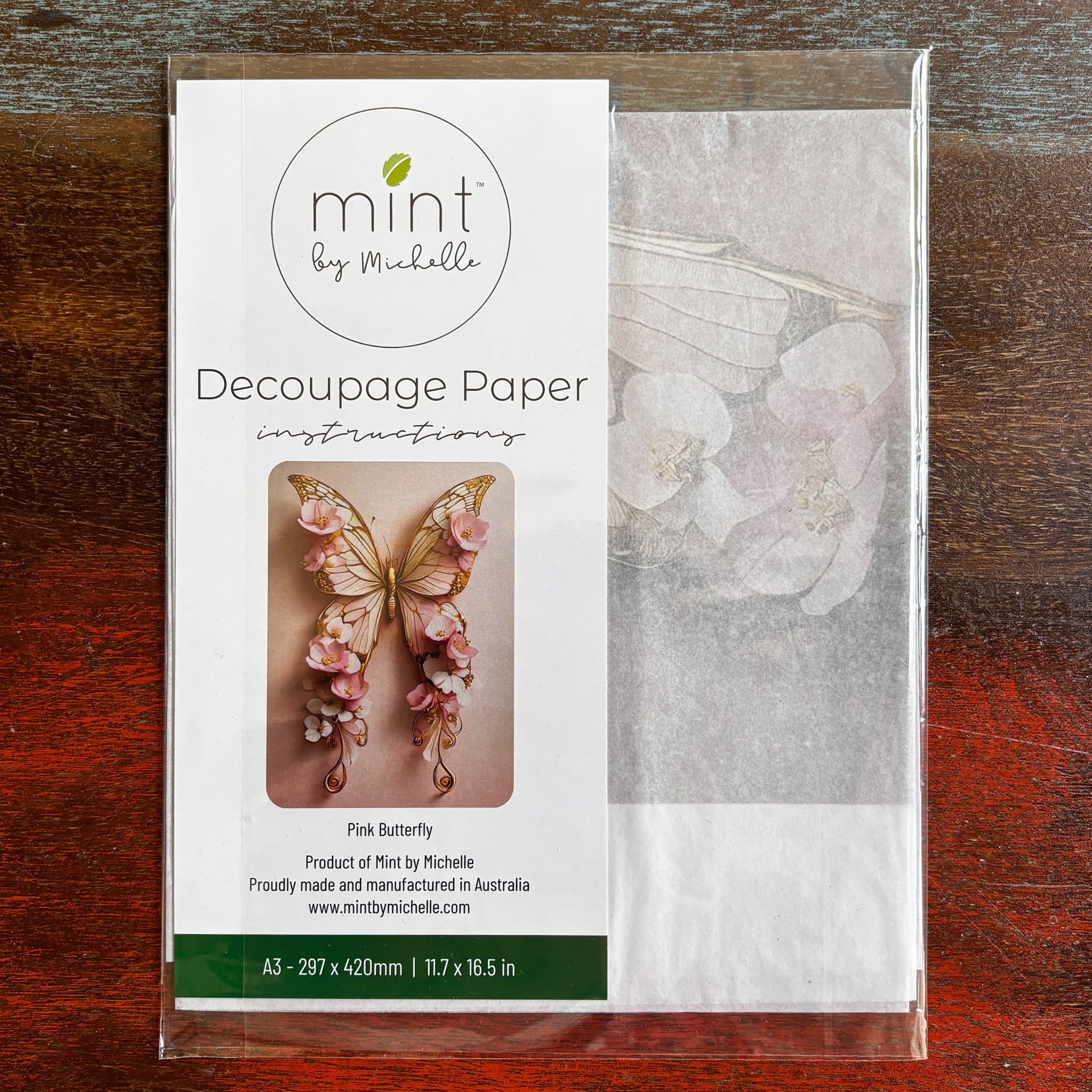 A package of Mint by Michelle's Pink Butterfly A3 decoupage paper is against a dark wood background.