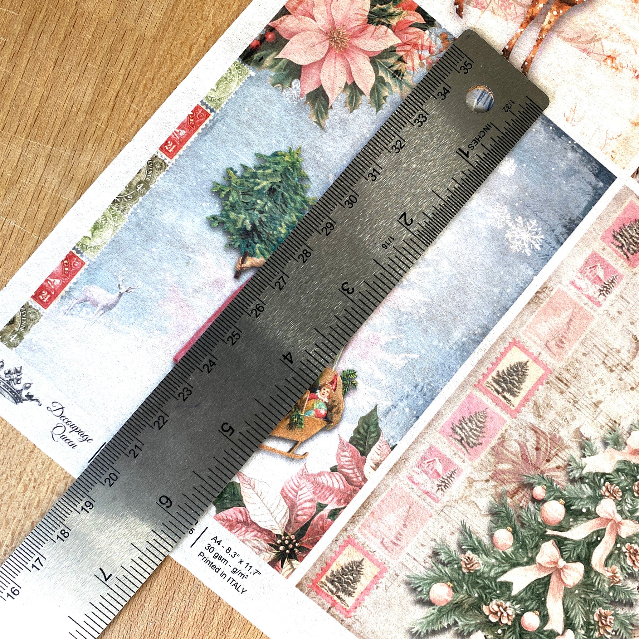 A close-up of Decoupage Queen's Four Pink Winter Scenes A4 rice paper shows a silver ruler over one of the designs showing a measurement of 5.75 inches high.