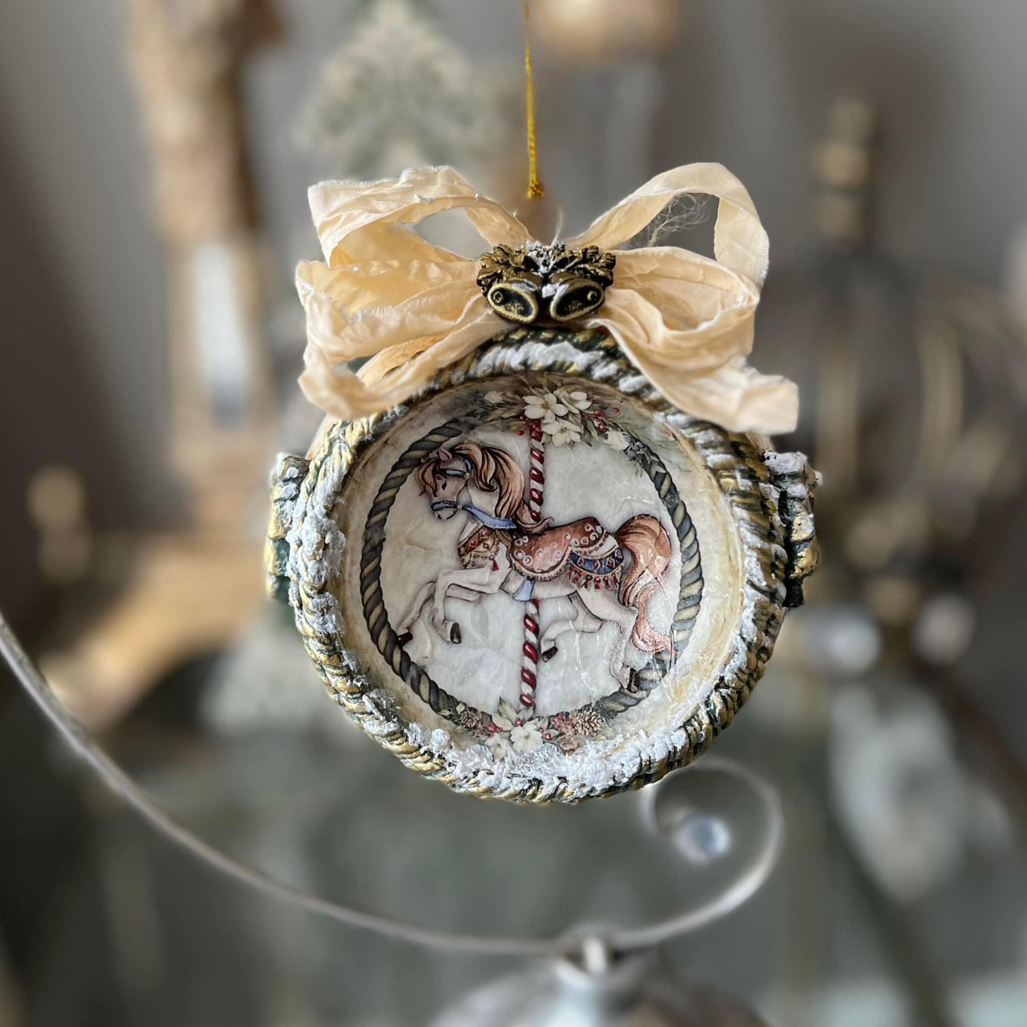 An ornament bauble with a concaved face features Decoupage Queen's Carousel 1 rice paper on it.