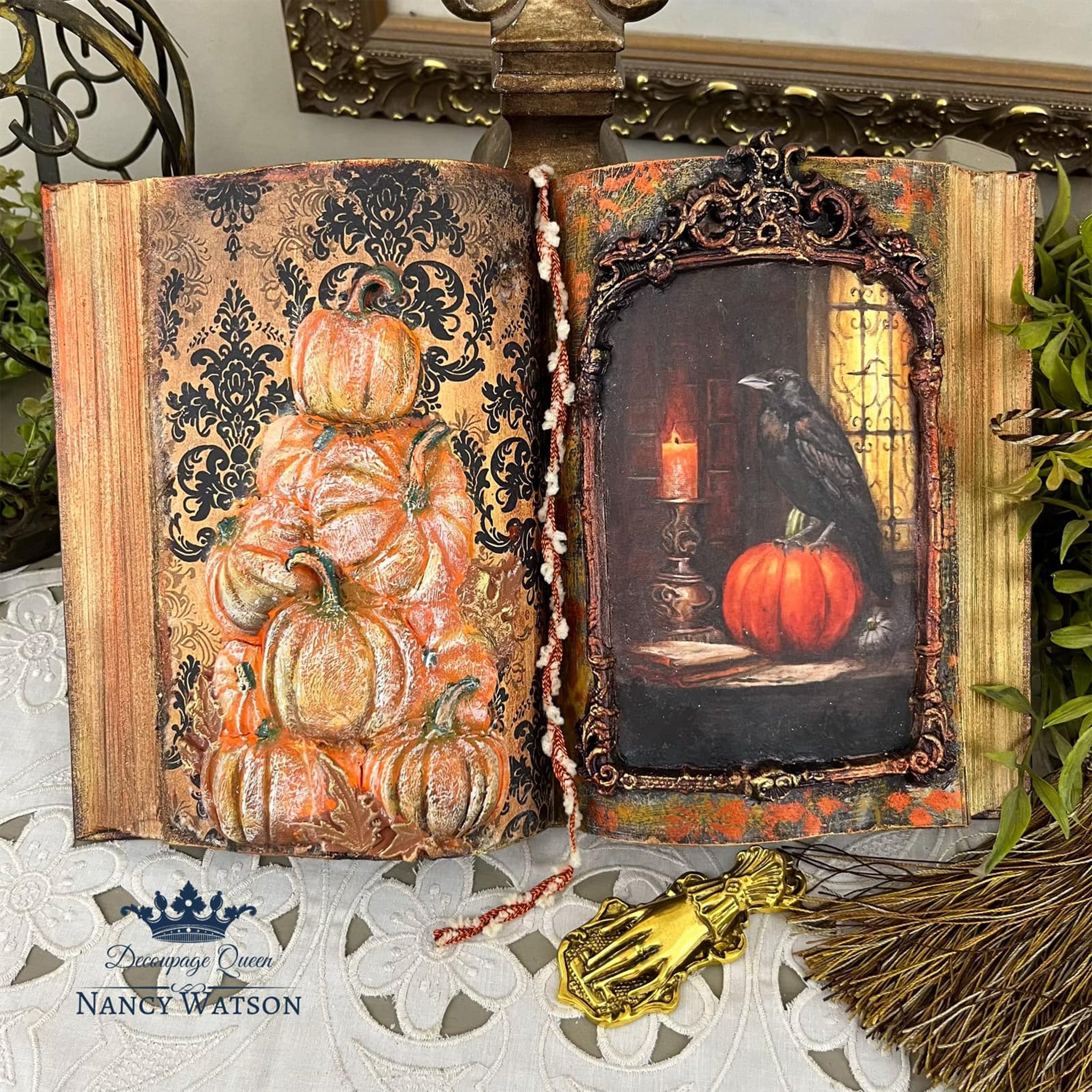 A book turned into decor features Decoupage Queen's Gothic Damask rice paper on it. Silicone mold castings of pumpkins sit against the rice paper.