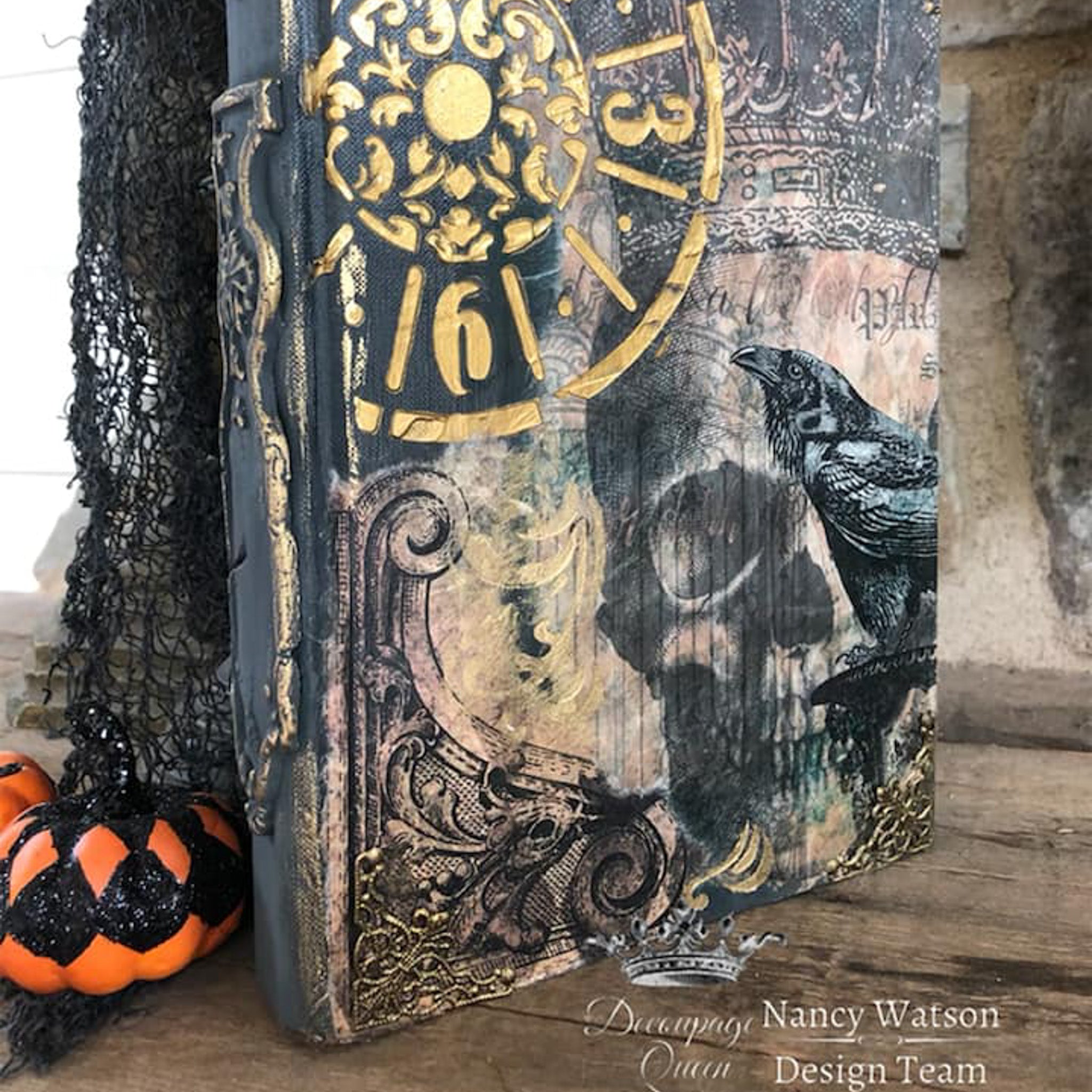 A close-up of a vintage book refurbished by Nancy Watson features Decoupage Queen's Halloween Raven with Skull and Gate on it.