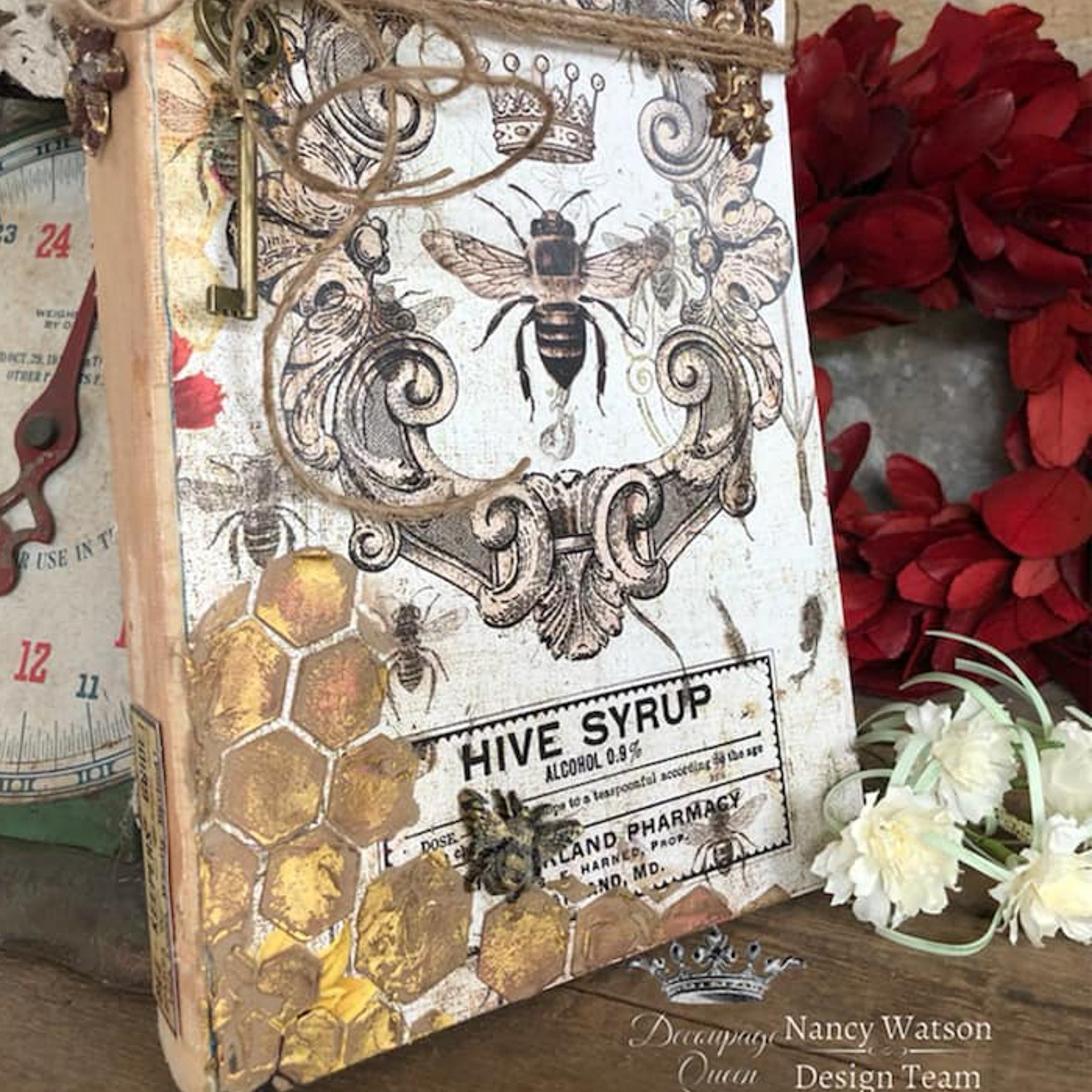 A vintage book refurbished by Nancy Watson Design Team features Decoupage Queen's Hive Syrup rice paper on it.