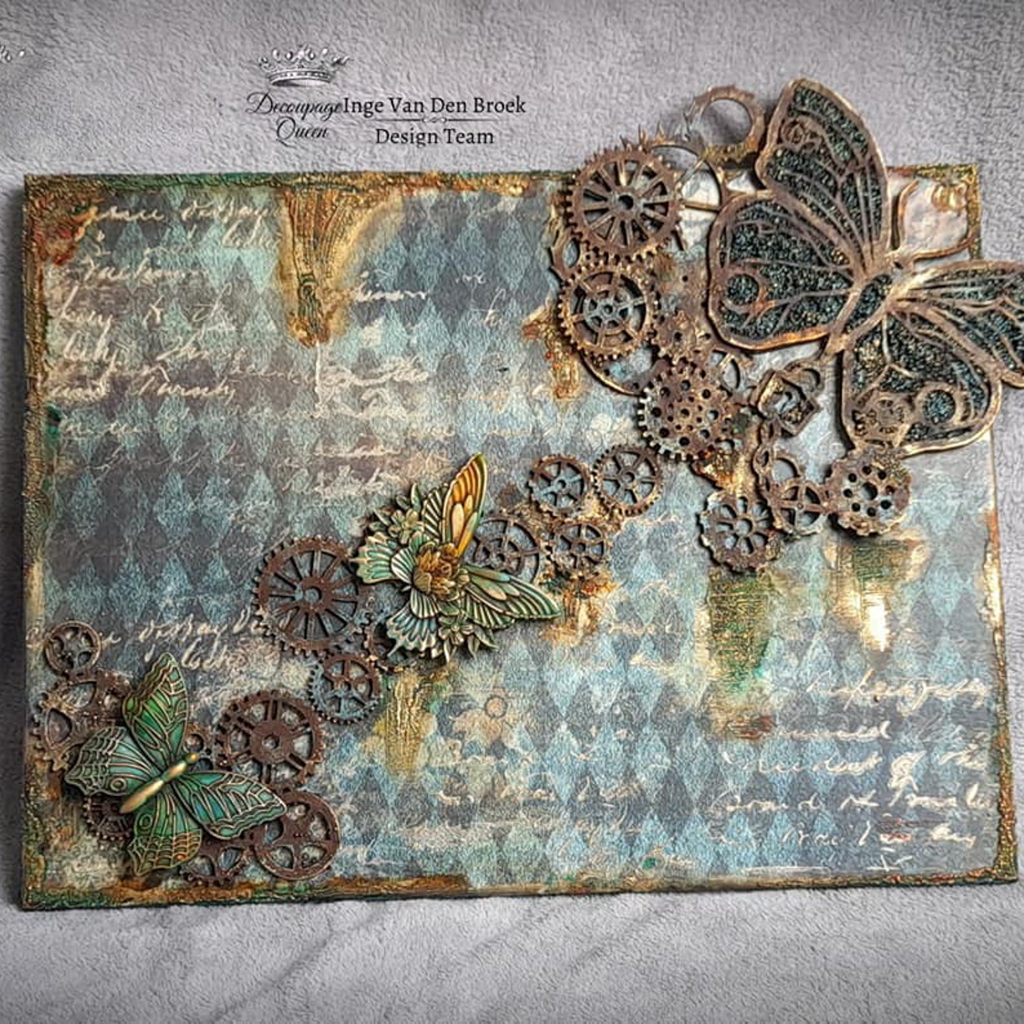 A metal plate craft created by Inge Van Den Broek has steampunk style butterflies and gears featured against Decoupage Queen's Teal Harlequin rice paper.