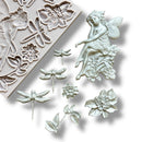 A light grey silicone mold and silver colored castings of a fairy sitting on a cluster of flowers, 2 single flowers, leaves, and 3 dragonflies are against a white background.