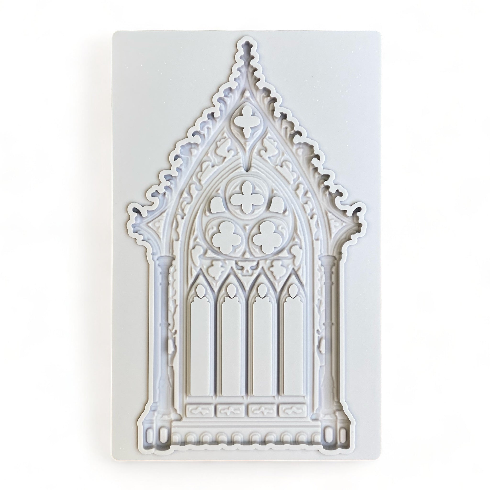 A light grey silicone mold of an ornate Gothic window is against a white background.