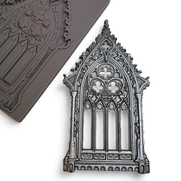 A brown silicone mold and silver colored casting of an ornate Gothic window are against a white background.
