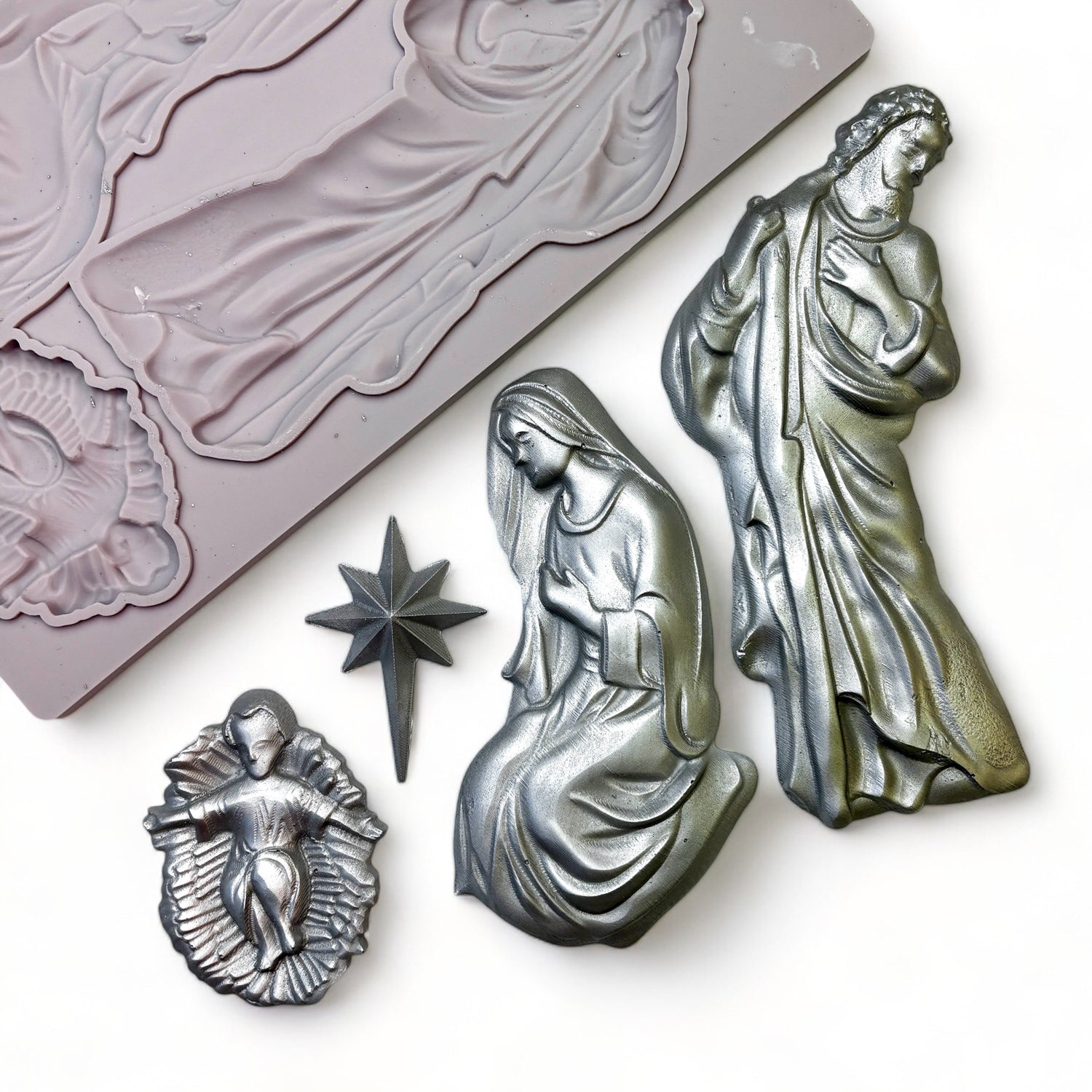 A beige silicone mold and silver colored castings of the Holy Family and the Bethlehem Star are against a white background.