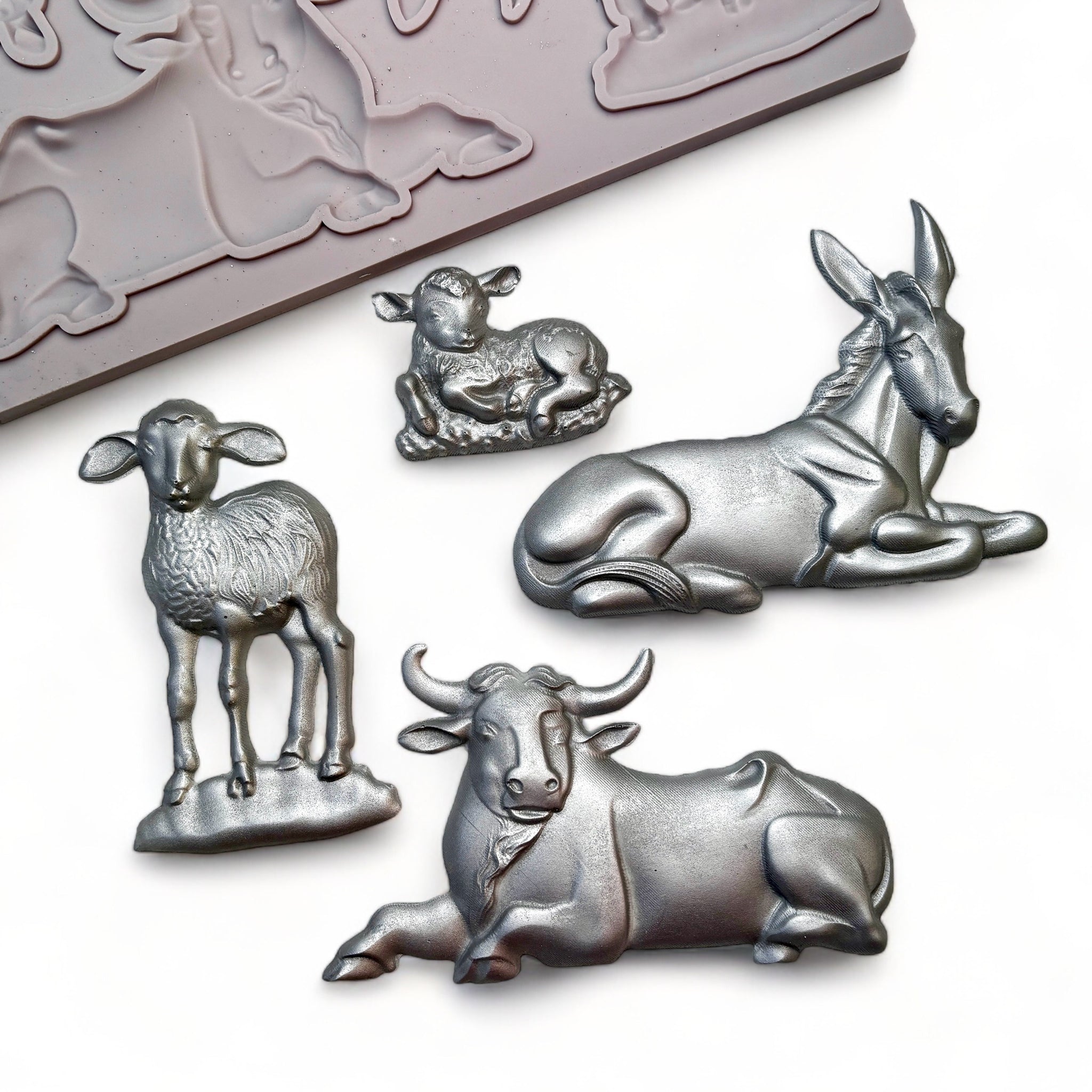 A beige silicone mold and silver colored castings of 4 nativity animals are against a white background.