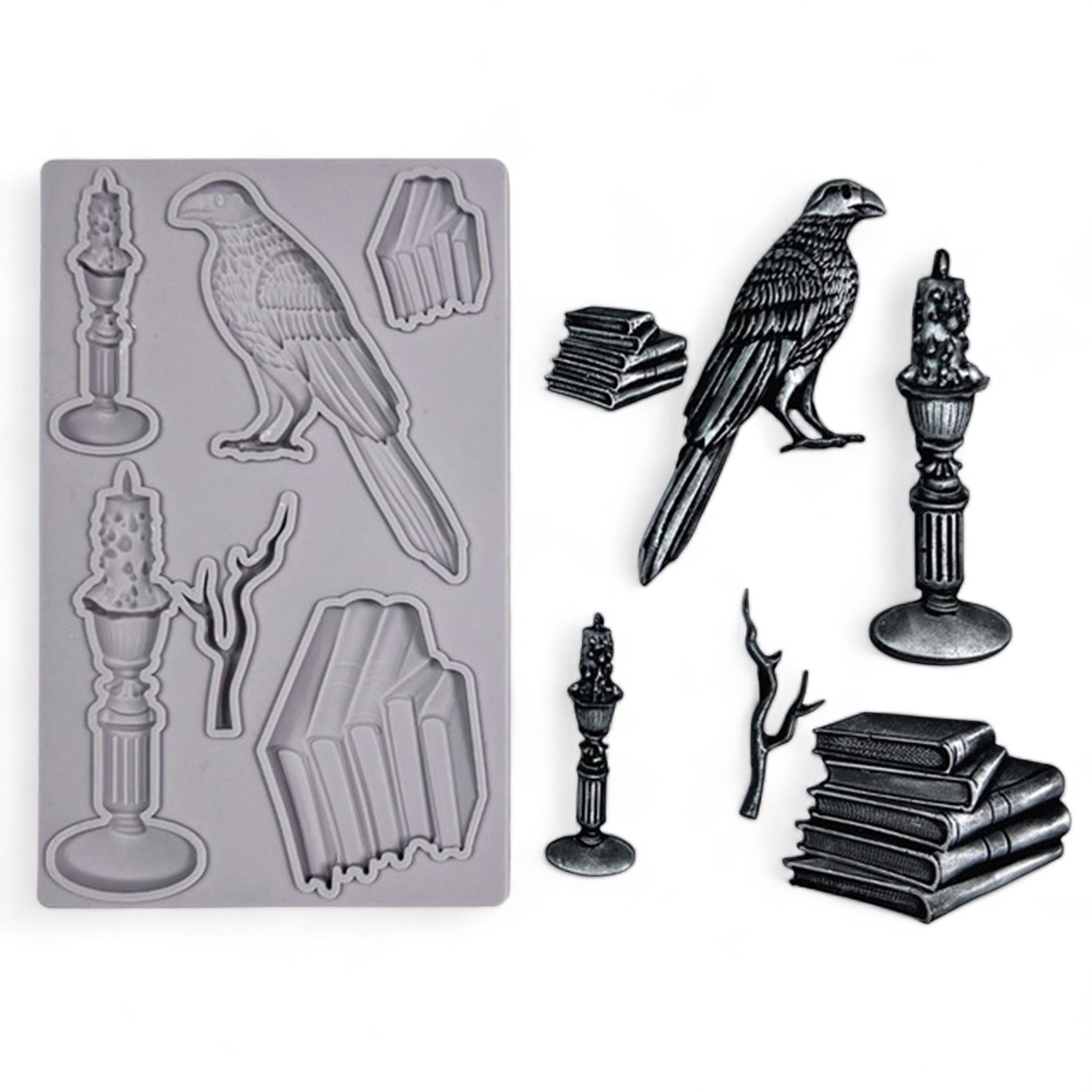 A light grey silicone mold and silver colored castings of stacks of books, candles, a branch, and a bird are against a white background. 