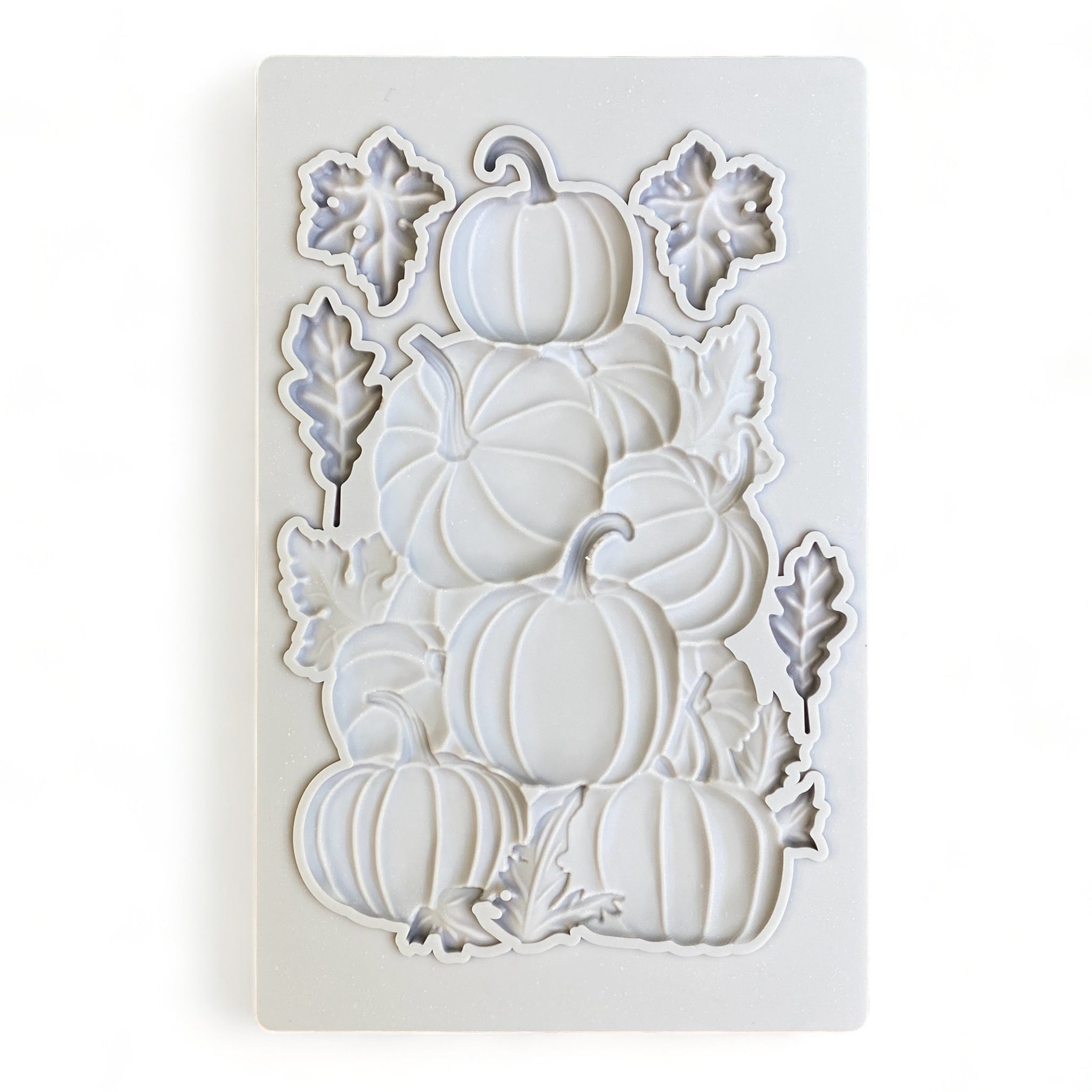 A grey silicone mold of a stack of pumpkins and 4 small loose leaves is against a white background.