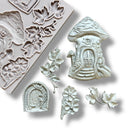 A light grey silicone mold and silver colored castings of a mushroom fairy house, a hobbit style door, and leaves and flowers are against a white background.