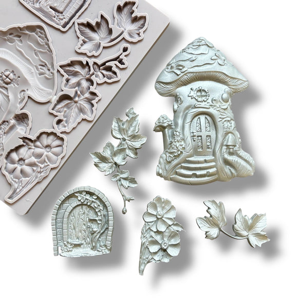 A light grey silicone mold and silver colored castings of a mushroom fairy house, a hobbit style door, and leaves and flowers are against a white background.
