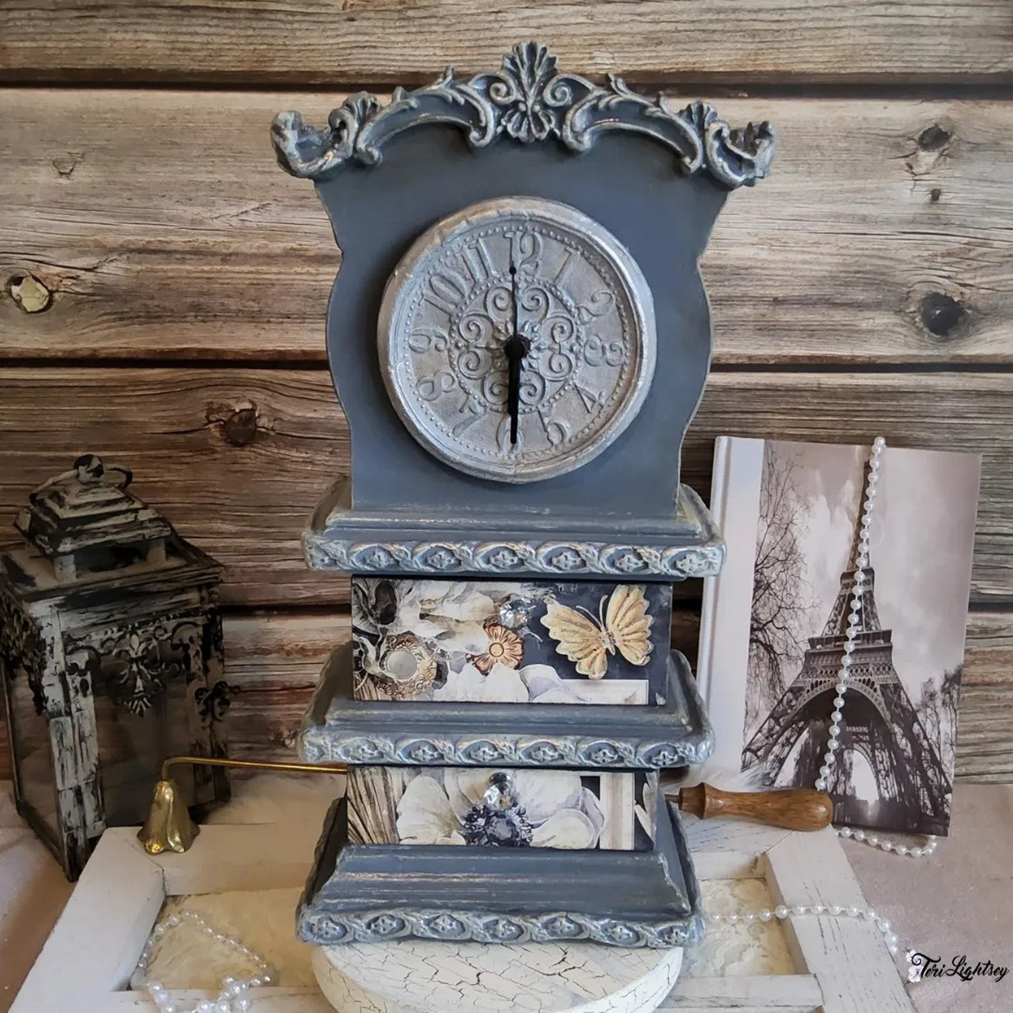 A vintage table clock with 2 drawers refurbished by Teri Lightsey is painted a muted blue and features Decoupage Queen's Sugar Magnolia A3 rice paper on the drawers.