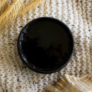 An arial view of an open container of Dixie Belle Paint Company's Anchor All-In-One Silk Paint is on a white knit material with golden wheat sprigs.