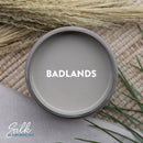 An arial view of an open container of Dixie Belle Paint Company's Badlands Silk All-In-One Mineral Paint is shown with white text reading Badlands