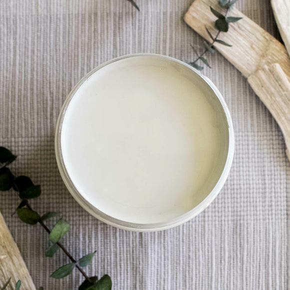 An arial view of an open container of Dixie Belle Paint Company's Baja Gray All-In-One Silk Paint is on a beige material with greenery and wood pieces.