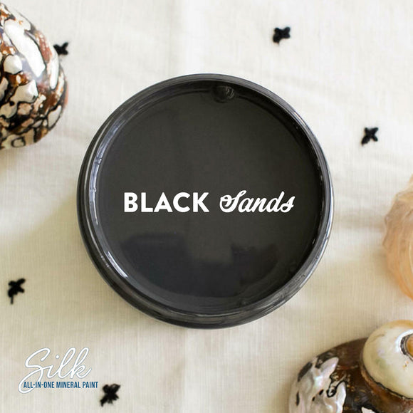 An arial view of an open container of Dixie Belle Paint Company's Black Sands Silk All-In-One Mineral Paint is shown with white text reading Black Sands.