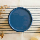 An arial view of an open container of Dixie Belle Paint Company's Cape Current All-In-One Silk Paint is on a white knit material with dark grey stripes.