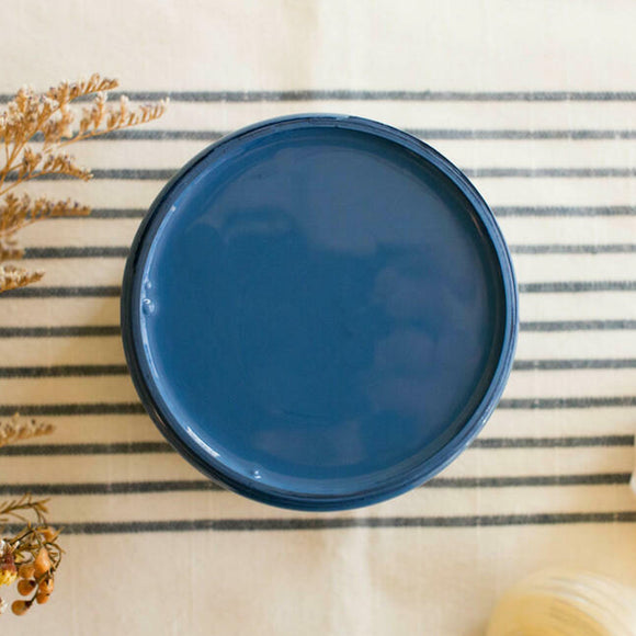 An arial view of an open container of Dixie Belle Paint Company's Cape Current All-In-One Silk Paint is on a white knit material with dark grey stripes.
