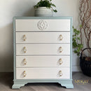 White dresser with gold handles in a room setting with plants and decor.