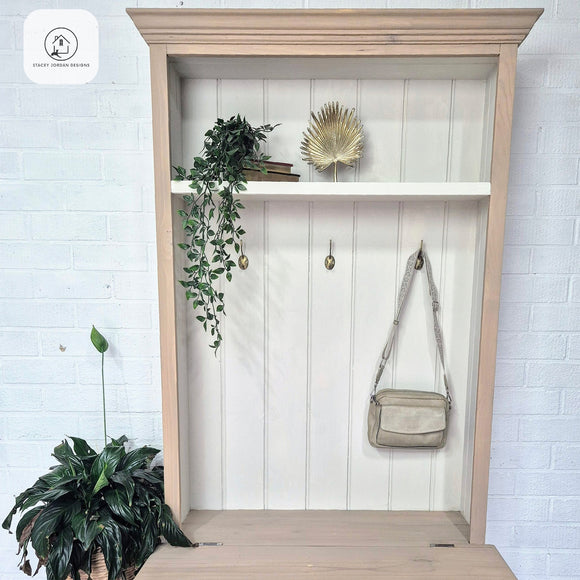 Wooden wardrobe with shelves, plants, and a handbag against a white brick wall.