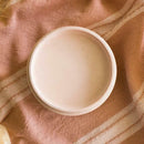 An arial view of an open container of Dixie Belle Paint Company's Conch All-In-One Silk Paint is on a pink material with 2 large white stripes with pink stitching.