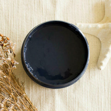 An arial view of an open container of Dixie Belle Paint Company's Deep Sea All-In-One Silk Paint is on a white material with a bleached starfish and dried beach flowers.