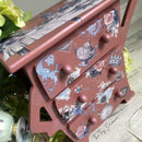 A quirky 3-drawer night stand refurbished by The Top Drawer features Dixie Belle's Desert Rose Silk All-In-One Mineral Paint and Alice in Wonderland rub-on transfers.