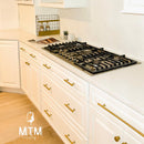 Modern kitchen with white cabinets, gold handles, and a gas stove.