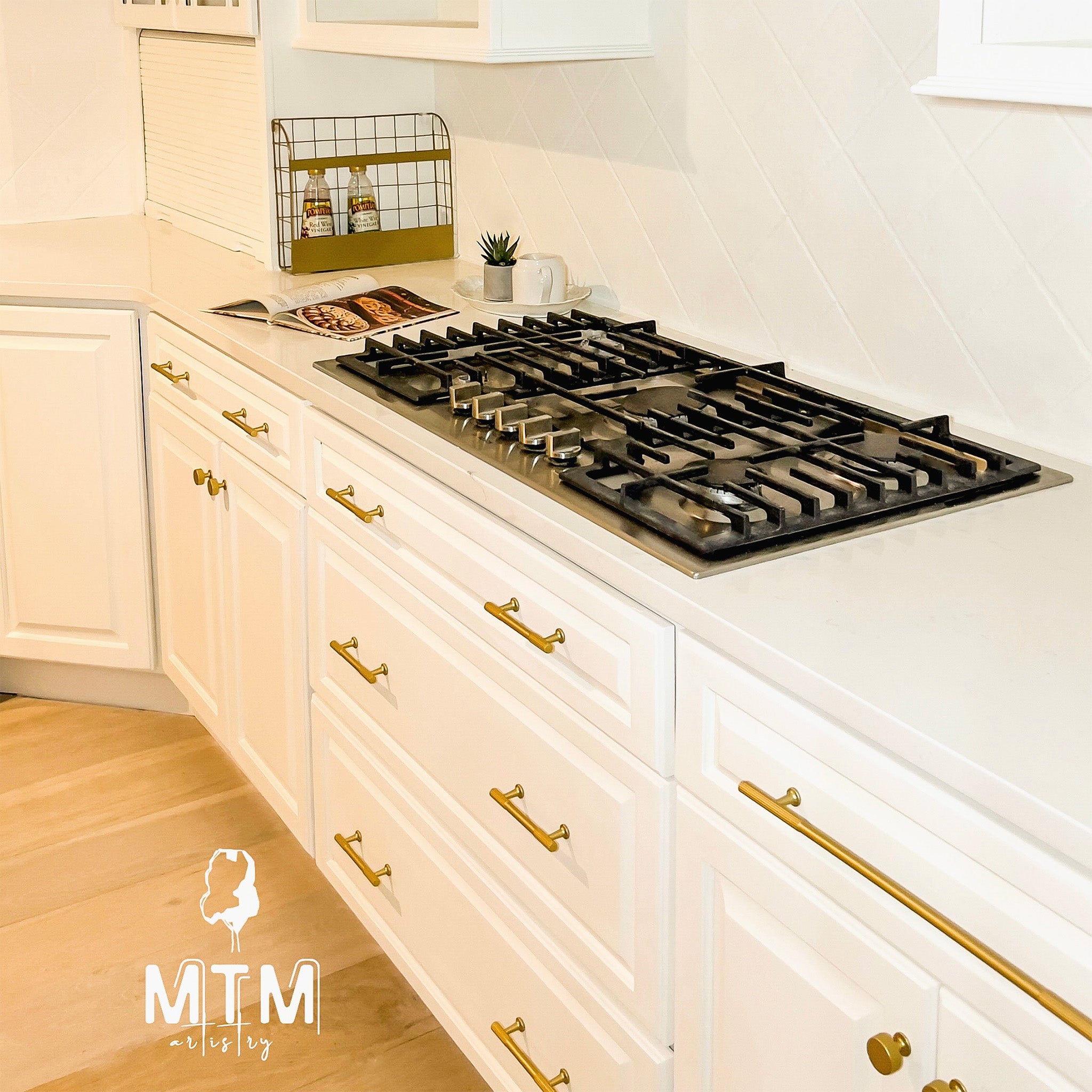 Modern kitchen with white cabinets, gold handles, and a gas stove.