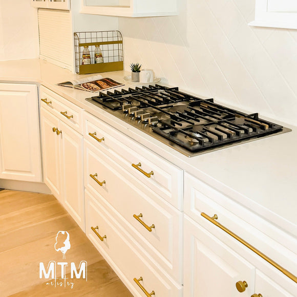 Modern kitchen with white cabinets, gold handles, and a gas stove.