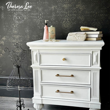 White dresser with decorative items against a dark wall with floral patterns, featuring the brand 'Theresa Lee'.