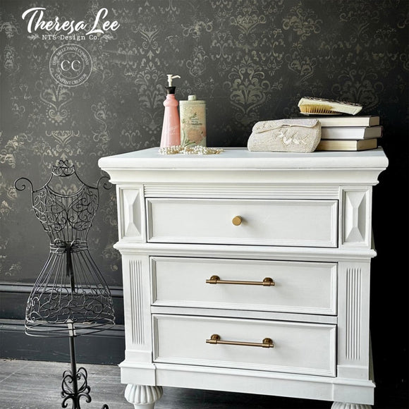 White dresser with decorative items against a dark wall with floral patterns, featuring the brand 'Theresa Lee'.