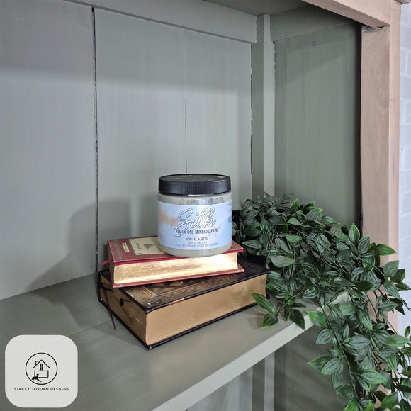 Candle on top of books with a plant nearby on a shelf