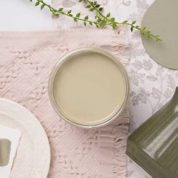 Jar of light-colored green paint on a textured surface with decorative elements